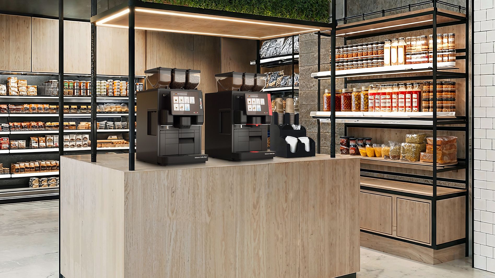 Zwei Schaerer Coffee Skye Kaffeemaschinen stehen einsatzbereit auf einer modernen Selbstbedienungstheke in einem stilvoll eingerichteten Geschäft, umgeben von Regalen mit Lebensmitteln und Snacks.