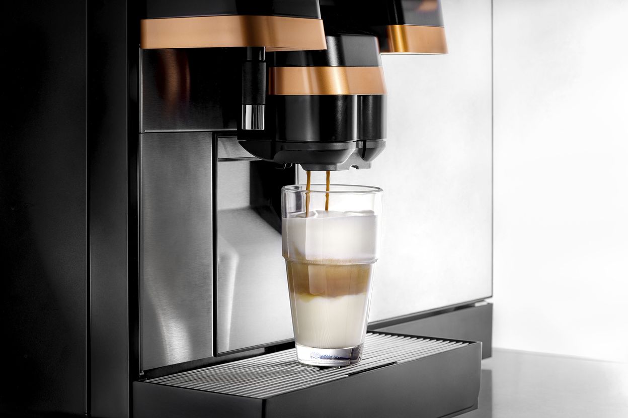 A sleek coffee machine brewing a layered latte into a glass, with a rich espresso stream and frothy milk, set on a modern countertop.