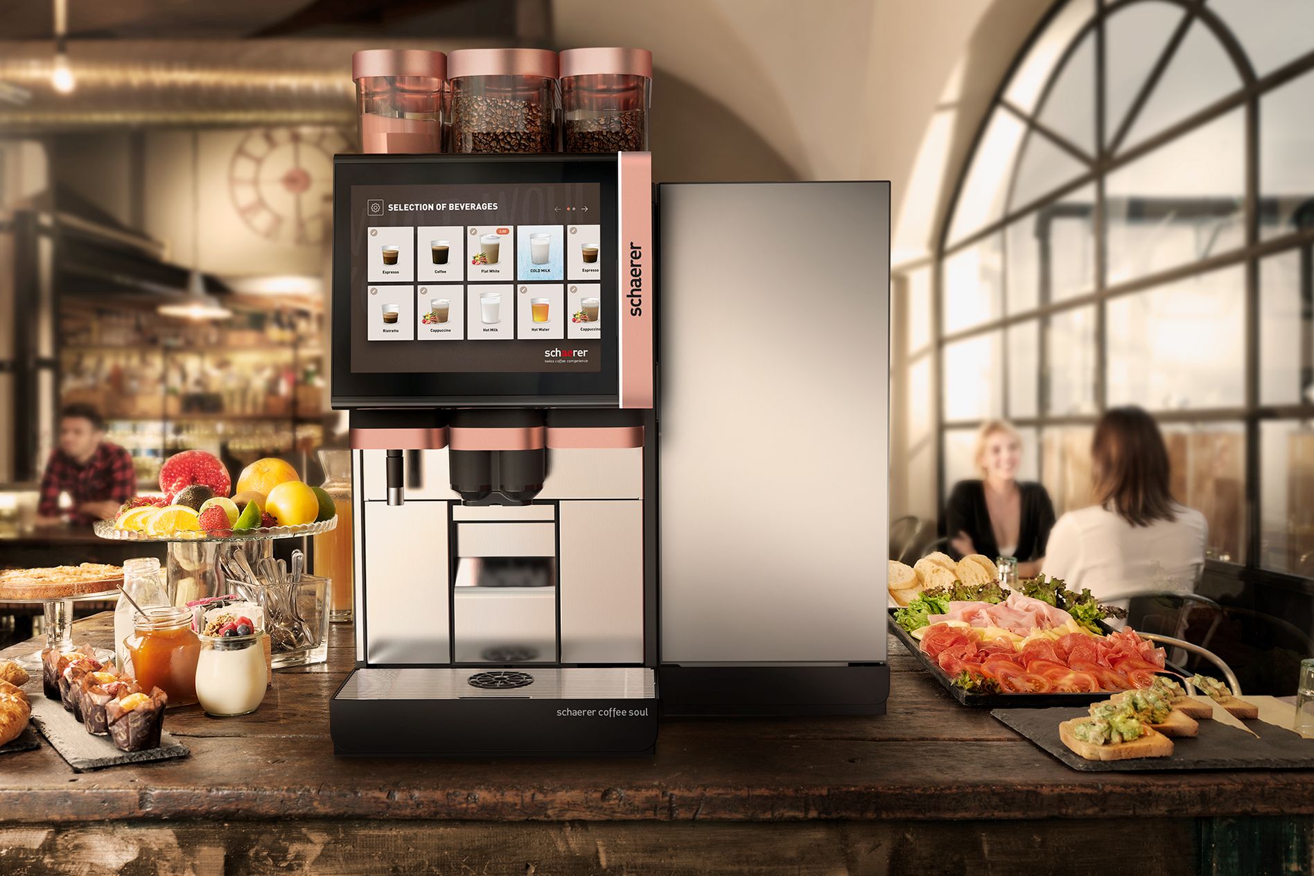 This image shows a Schaerer Coffee Soul machine prominently displayed in a café or restaurant setting. The coffee machine features a sleek, modern design with multiple bean hoppers and a large, intuitive touchscreen interface. The surroundings include a rustic wooden table loaded with various food items, such as fresh fruits, pastries, meats, cheese, and bread, suggesting a high-quality food service environment. In the background, patrons are seated, enjoying their time, which reinforces a warm and inviting atmosphere. The design of the machine and the aesthetic of the café reflect Schaerer's emphasis on flexibility, coffee competence, and premium quality.