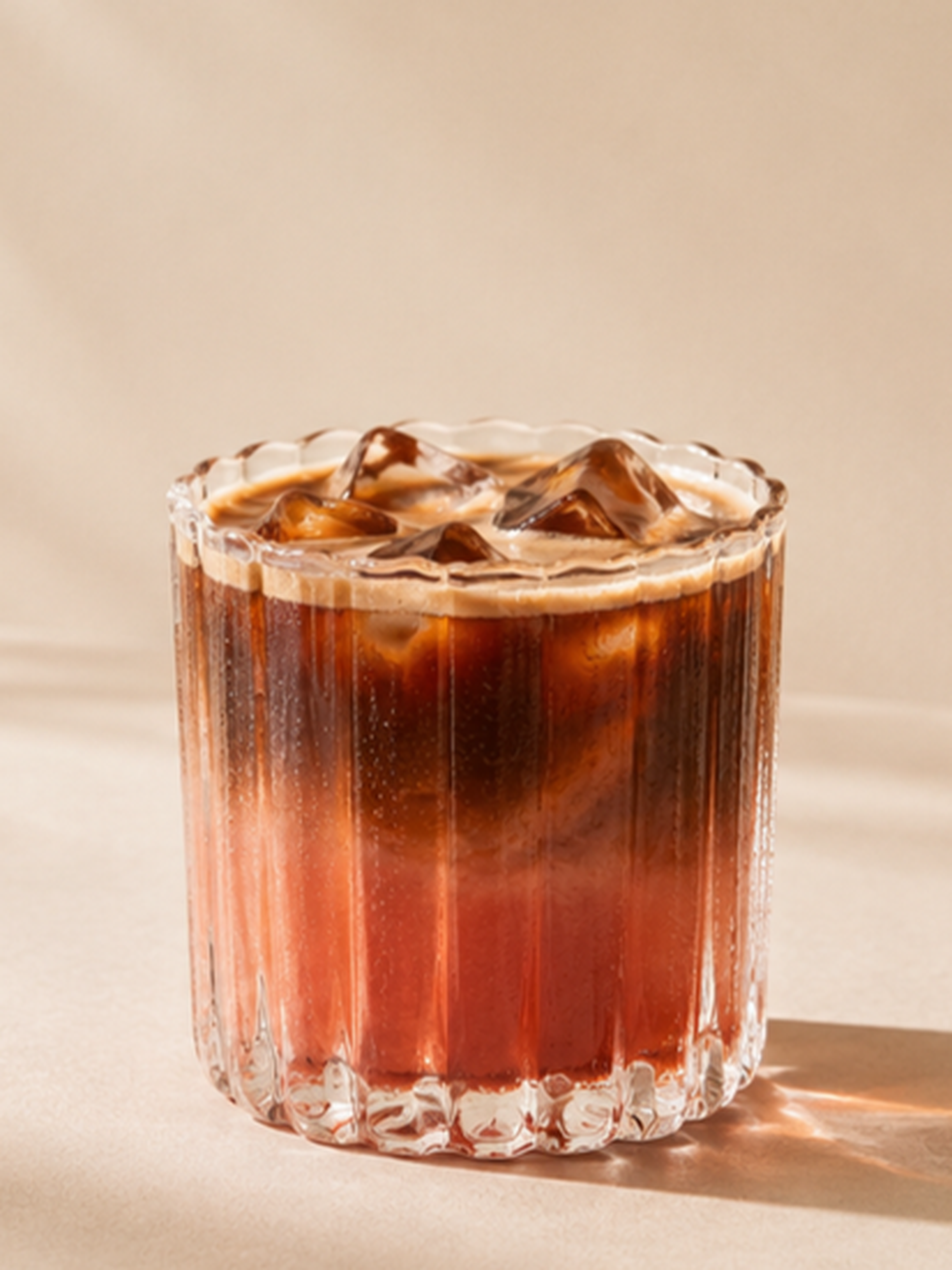 A glass of iced coffee with a creamy swirl on top, served in a ribbed tumbler against a neutral background.