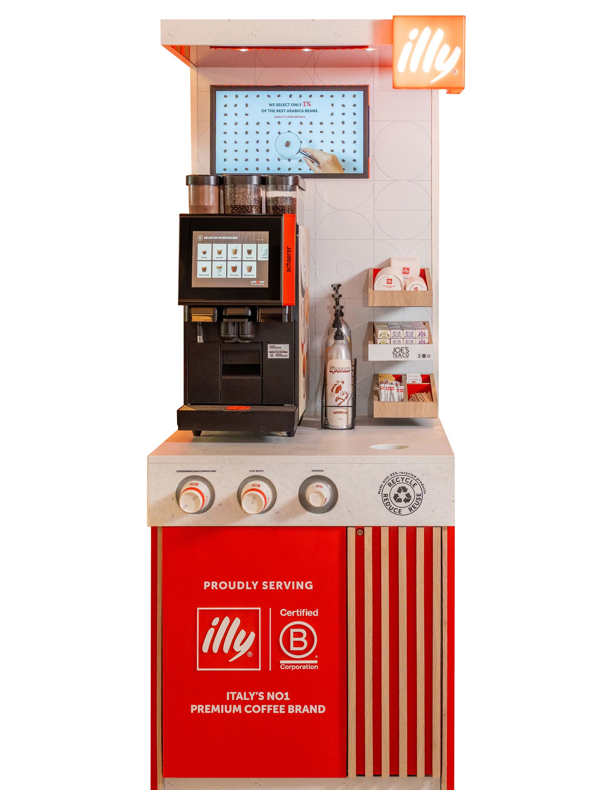 Front view of the illy “on the go” coffee station with a Schaerer coffee machine, digital display, cup and accessory shelves, syrup bottle, branded counter controls and prominent illy and B Corp branding.