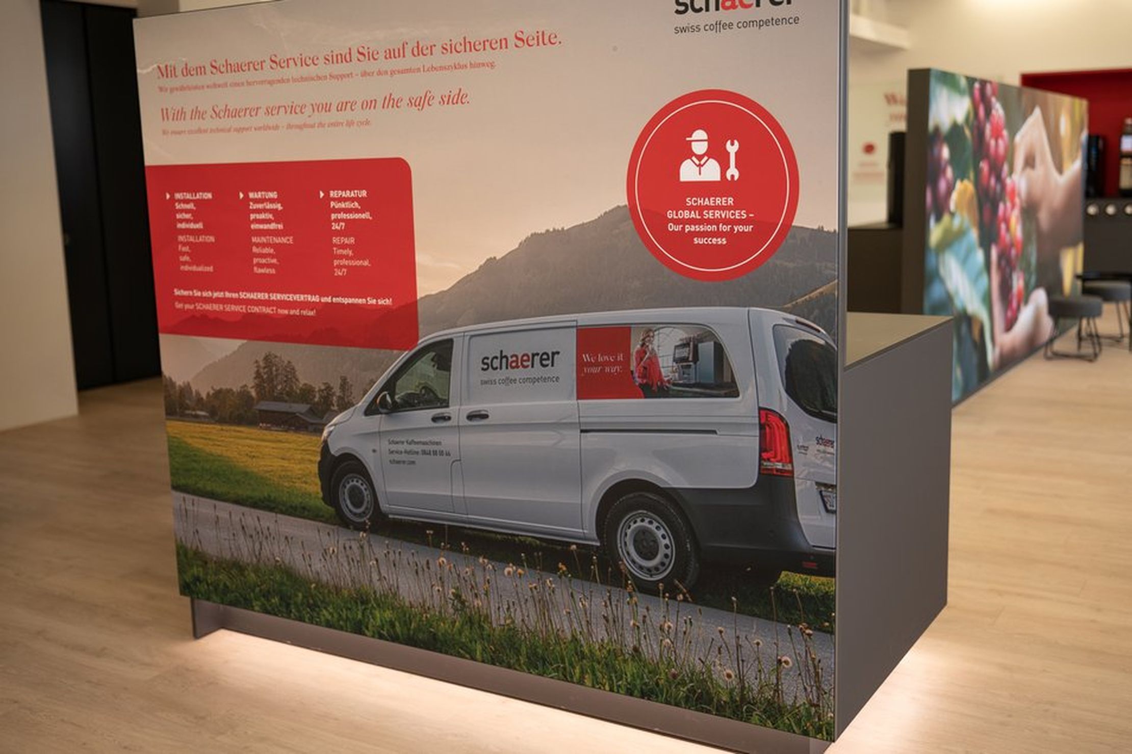 Display with a Schaerer service van image, highlighting global services for coffee competence, in a modern showroom setting.
